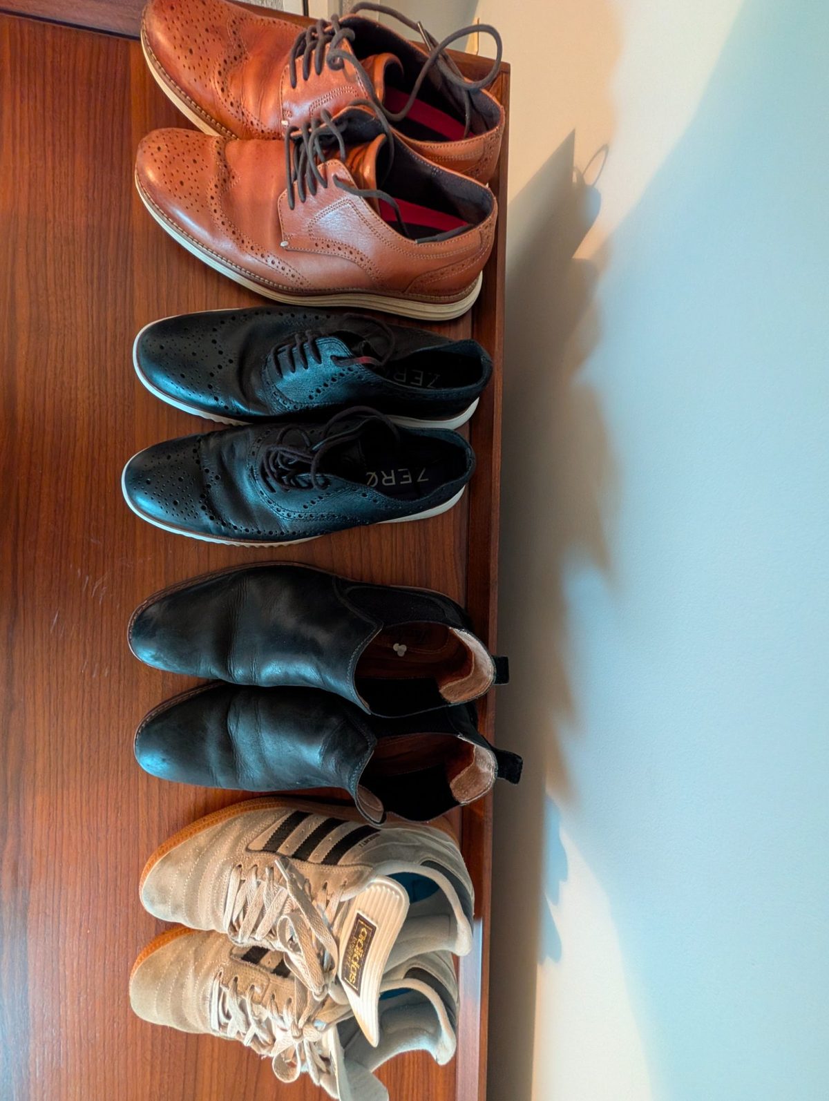 Four pairs of shoes arranged from most to least formal: tan leather wingtip brogue, black leather wingtip brogue, black Chelsea boot, and grey Adidas sneaker